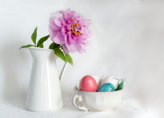 Easter still life with gorgeous pink peonies in a vase and an antique porcelain bowl with coloured eggs on a white background