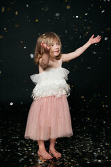 joyful smiling beautiful girl in ballerina dress with confetti in a studio with black backdrop