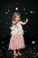 Fototapeta premium little girl in a dress playing with confetti against black backdrop