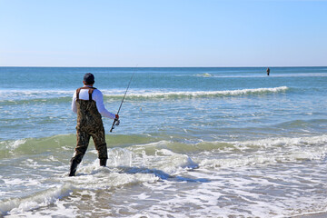 Fisherman heading out for winter surf fishing from the beach. - obrazy, fototapety, plakaty