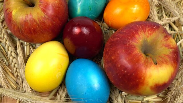 Colored Easter eggs with wheat ears, fresh ripe apples and composition of dried ears of wheat on the wooden board, background.  Happy Easter