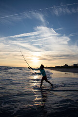 Silhouette of a surf fisherman casting a fishing rod at sunset.