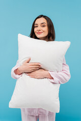 Fototapeta premium pleased young woman in sleepwear holding white pillow isolated on blue.