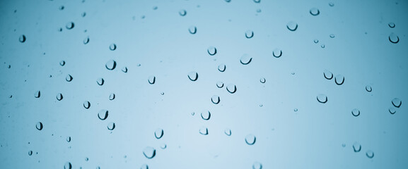 Minimal light backdrop with rain droplets on white glass. Light wet window with rainy drops closeup in blue light. Blurry minimalist monochrome background of window glass with raindrops close up.