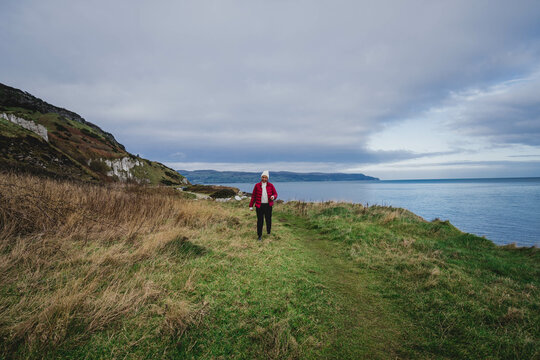 Path Glenarm Coastal Path, south of the village of Glenarm, in Northern Ireland,  with woman hiker in red jacket