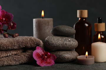 Fototapeta na wymiar Beautiful composition with burning candles, spa stones and different care products on dark grey table, closeup