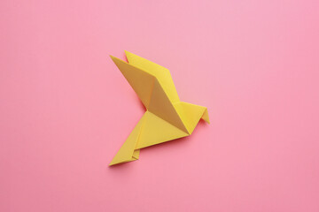 Beautiful yellow origami bird on pink background, top view