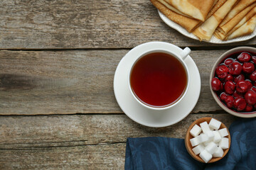 Cup of tea, cherry and crepes on wooden table, flat lay. Space for text