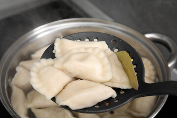 Fototapeta na wymiar Dumplings (varenyky) with tasty filling on skimmer over pot indoors, closeup