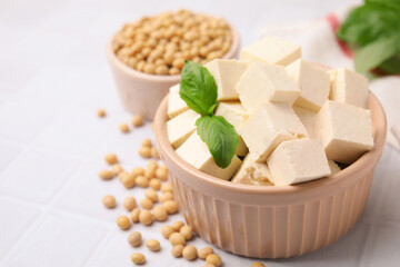Delicious tofu cheese, basil and soybeans on white tiled table, closeup. Space for text
