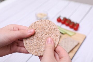 Woman holding tasty crispbread at white wooden table, closeup
