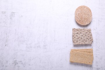 Different types of tasty crispbreads on white textured table, flat lay. Space for text