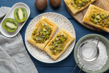 Fresh tasty puff pastry with kiwi served on blue wooden table, flat lay
