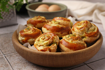 Fresh delicious puff pastry with tasty filling in wooden bowl on white tiled surface, closeup