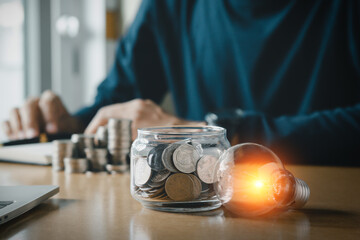 Businessman holding and putting lightbulb on coins stack on table for saving energy and saving money concept.