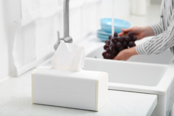 Woman washing grapes with running water over sink in kitchen, focus on paper towels. Space for text