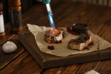 Cooking meat medallions with manual gas burner on wooden table in photo studio. Food stylist
