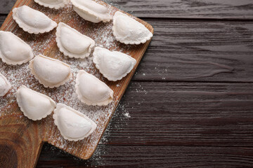 Raw dumplings (varenyky) on brown wooden table, top view. Space for text