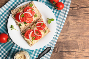Fresh crunchy crispbreads with pate, tomatoes, red onion and greens on wooden table, flat lay. Space for text