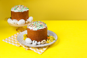 Traditional Easter cakes with sprinkles, painted eggs and beautiful spring flowers on yellow background, space for text