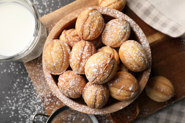Delicious nut shaped cookies with powdered sugar and milk on black table, flat lay