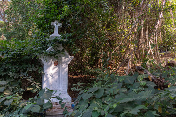 An old white cross surrounded by trees and woods in the Altinho area of the city of Panjim in Goa.