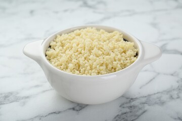 Bowl of tasty couscous on white marble table, closeup