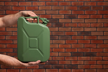 Man holding khaki metal canister against brick wall, closeup. Space for text