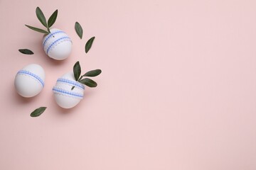 Beautifully decorated Easter eggs and green leaves on pale pink background, flat lay. Space for text