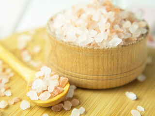 Fototapeta na wymiar Wooden spoon and bowl with large crystals of pink Himalayan salt on a white wooden background...