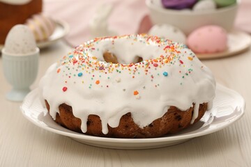 Delicious Easter cake decorated with sprinkles near painted eggs on white wooden table, closeup