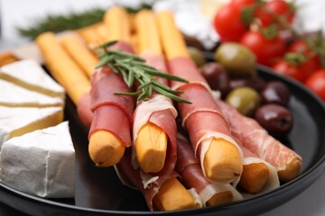 Delicious grissini sticks with prosciutto, cheese and olives on table, closeup