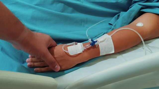Holding Patient's Hand on Hospital Bed with Medication Infusion