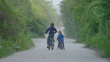 Two children riding bicycles on foggy and empty road, brother activities, nature