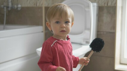 Funny little child cleaning and making mess with brush, cleaning toilet
