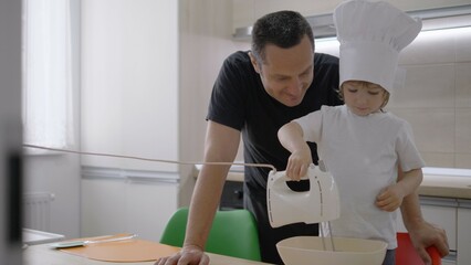 Obraz premium Father and son cook together, bay with cook hat blending with mixer ingredients