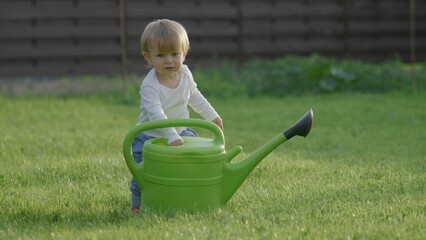 Amusing baby child look in a big watering can, kid put his hand in sprinkle