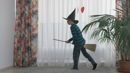 Child with wizard cap and broom play indoor, boy have fun home