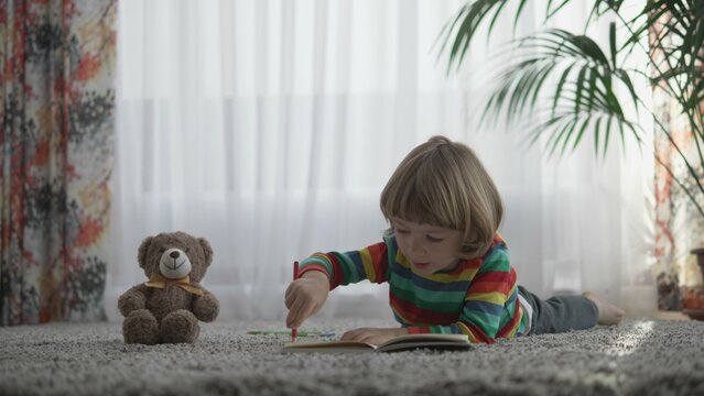 Adorable kid lying on floor and drawing near his teddy bear