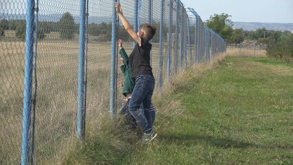 Three children wants to climb a big fence, brothers active in nature