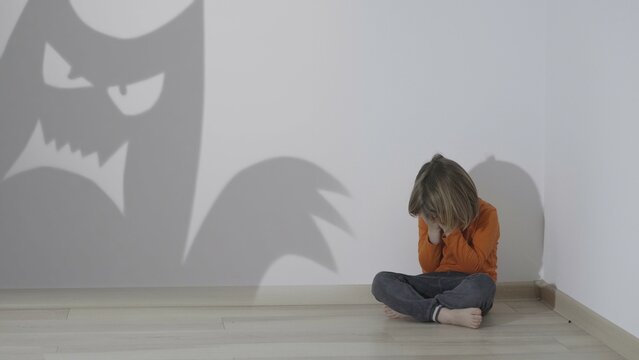 Child sitting alone in a corner, monster shadow silhouettes on wall, fears come to life, release, conceptual