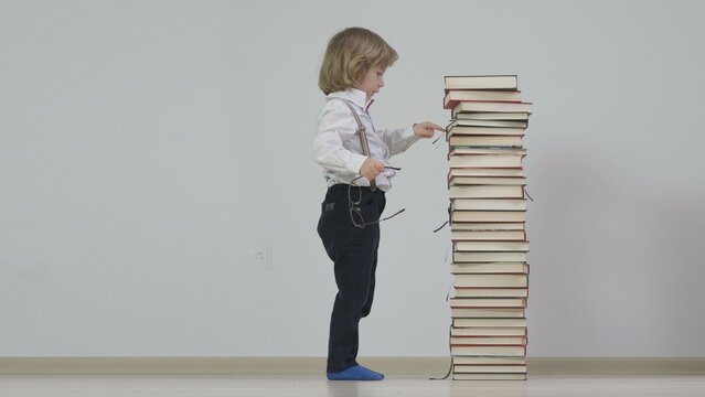 Little blond child with glasses counting the books in a tall pile