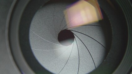 Front close-up view of camera lens diaphragm blades smoothly opening
