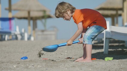 Little blonde hair child digs with shovel, beach and seaside