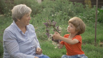 Little blonde hair child arrange flower crown to old grandmother, laughing faces