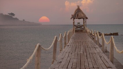 Fototapeta premium Wooden pontoon with end hut into the sea at sunrise over island