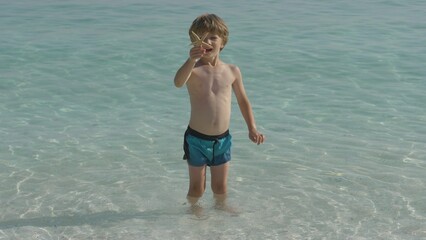 Cute little boy happy to find a starfish in the shallow sea water near the beach