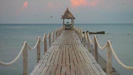 Naklejka premium Wooden pontoon with end hut into the sea at sunrise