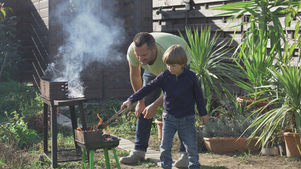 Man teaches son to prepare grill fire for the backyard barbecue