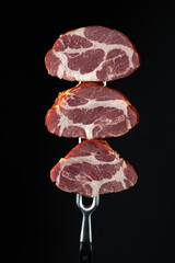 Sliced smoked steaks on a fork. Natural product from an organic farm. Menu for hotel on black background